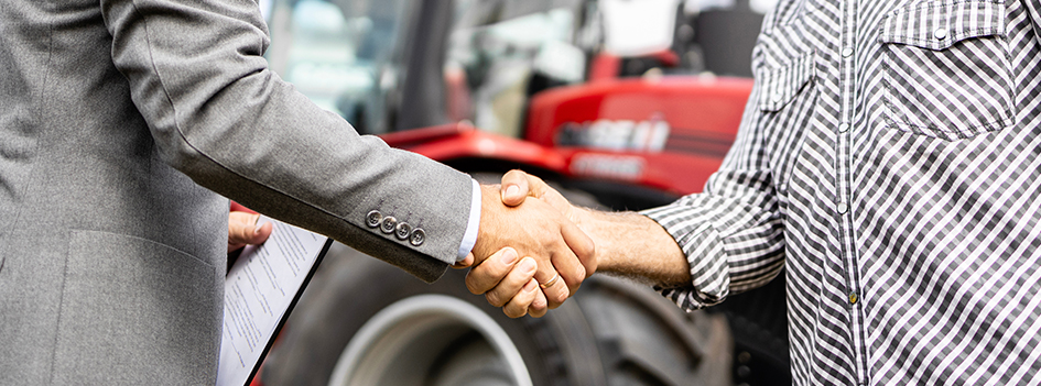 Buying new tractor agricultural machine. Close up view of buyer and dealer handshake at tractor dealership.