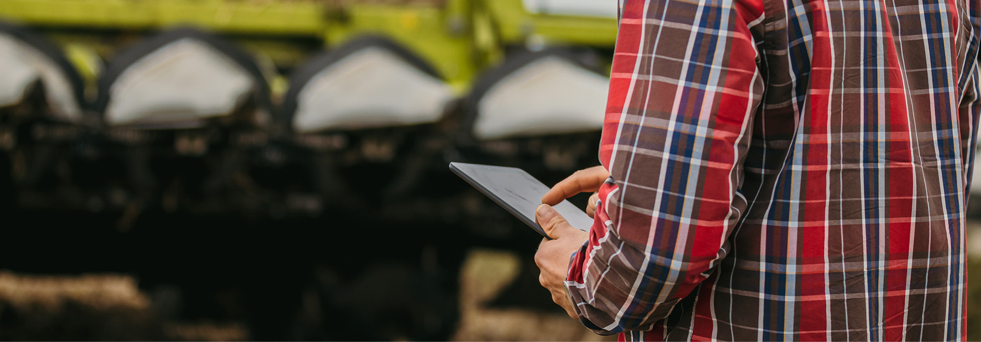Close-up of farmer looking at his Tablet, standing in front of a combine Harvester